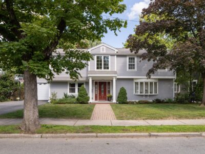Front exterior of renovated 4-bedroom colonial at 69 Hanson Road, Newton with grey siding, red door, walkway and mature trees